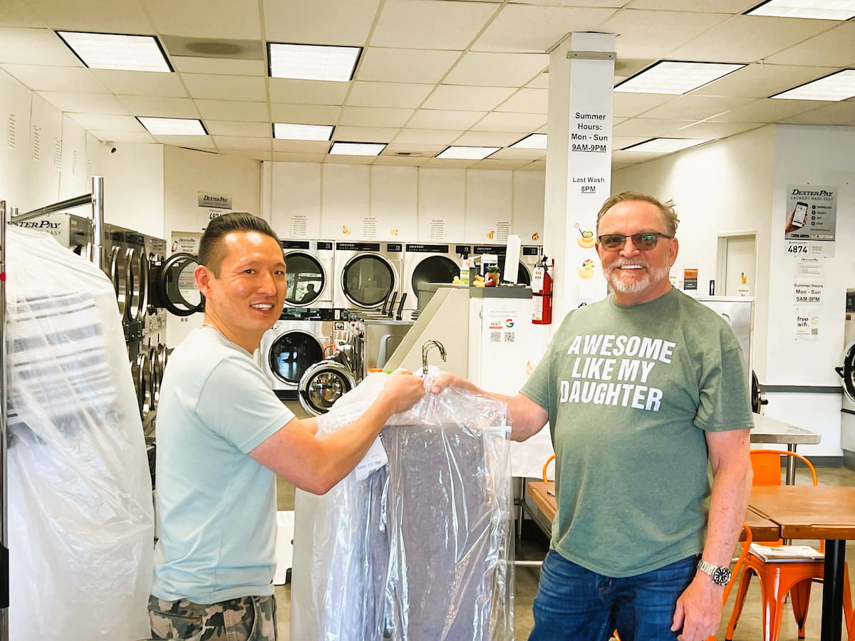 Owner of Bims Laundry Café handing dry cleaned clothes to a happy customer in Everett, WA