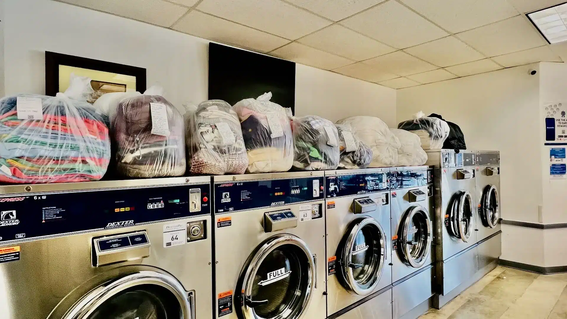 Stacked janitorial cleaning cloths and bagged laundry on a row of Dexter commercial washers at Bims Laundry Cafe in Everett, WA